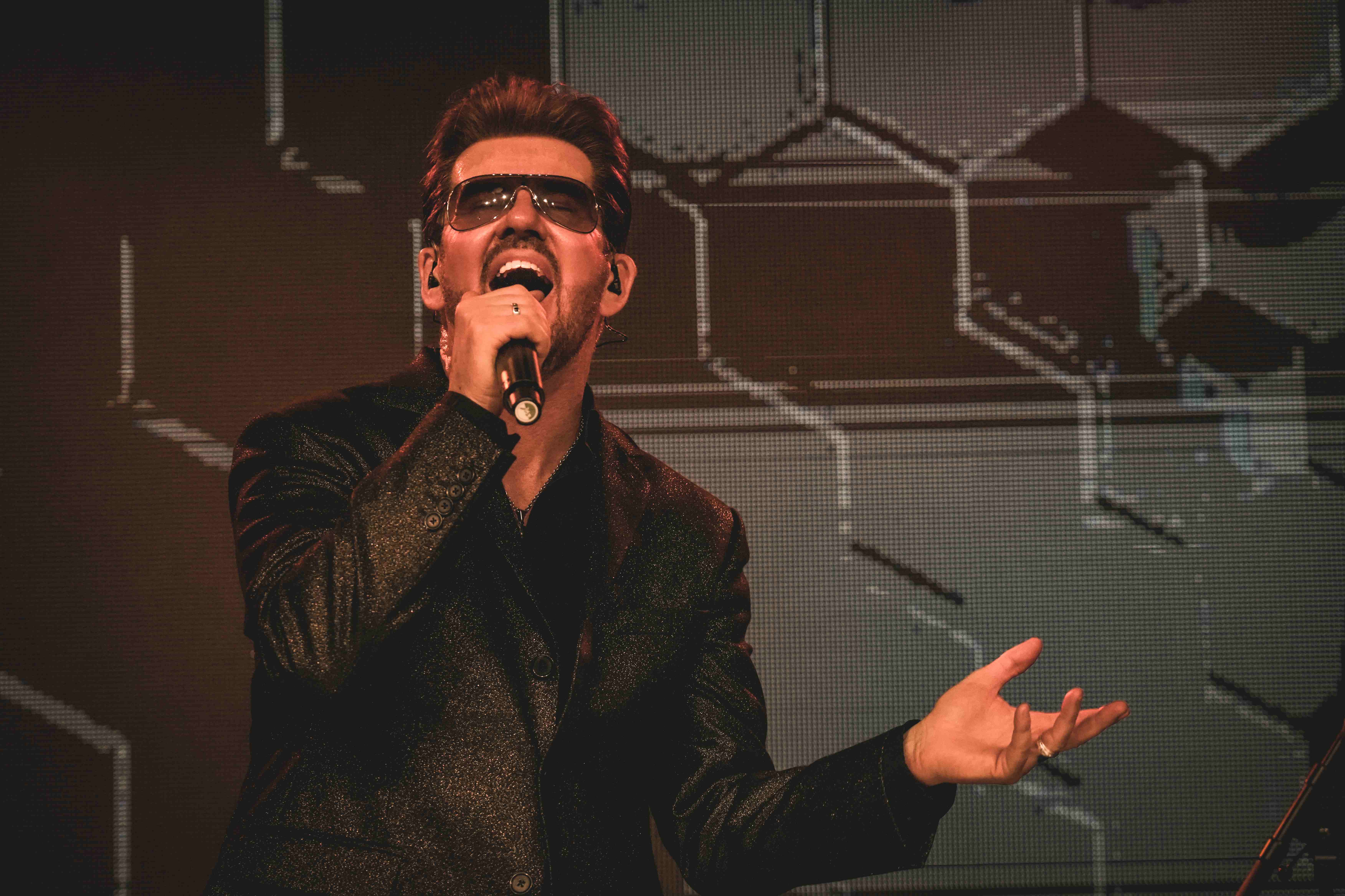 Steve Mitchell performing passionately with sunglasses against brown backdrop