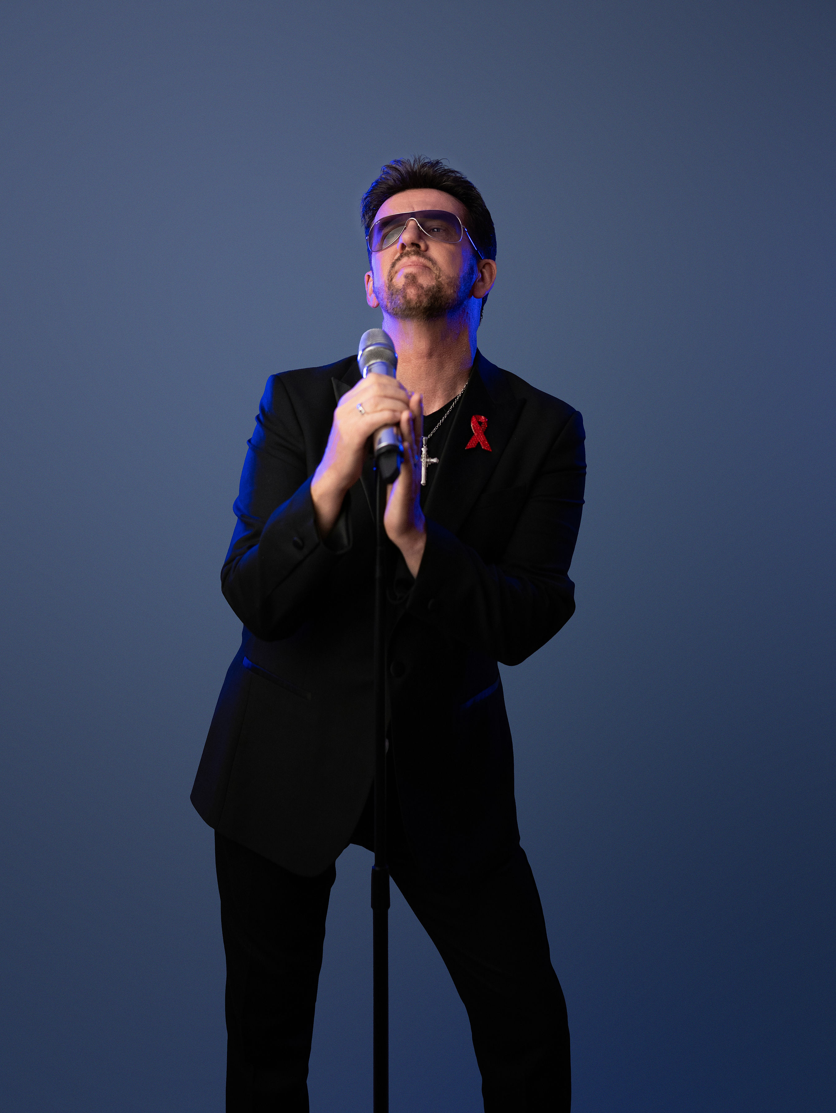 Steve Mitchell with hands clasped on microphone against blue background