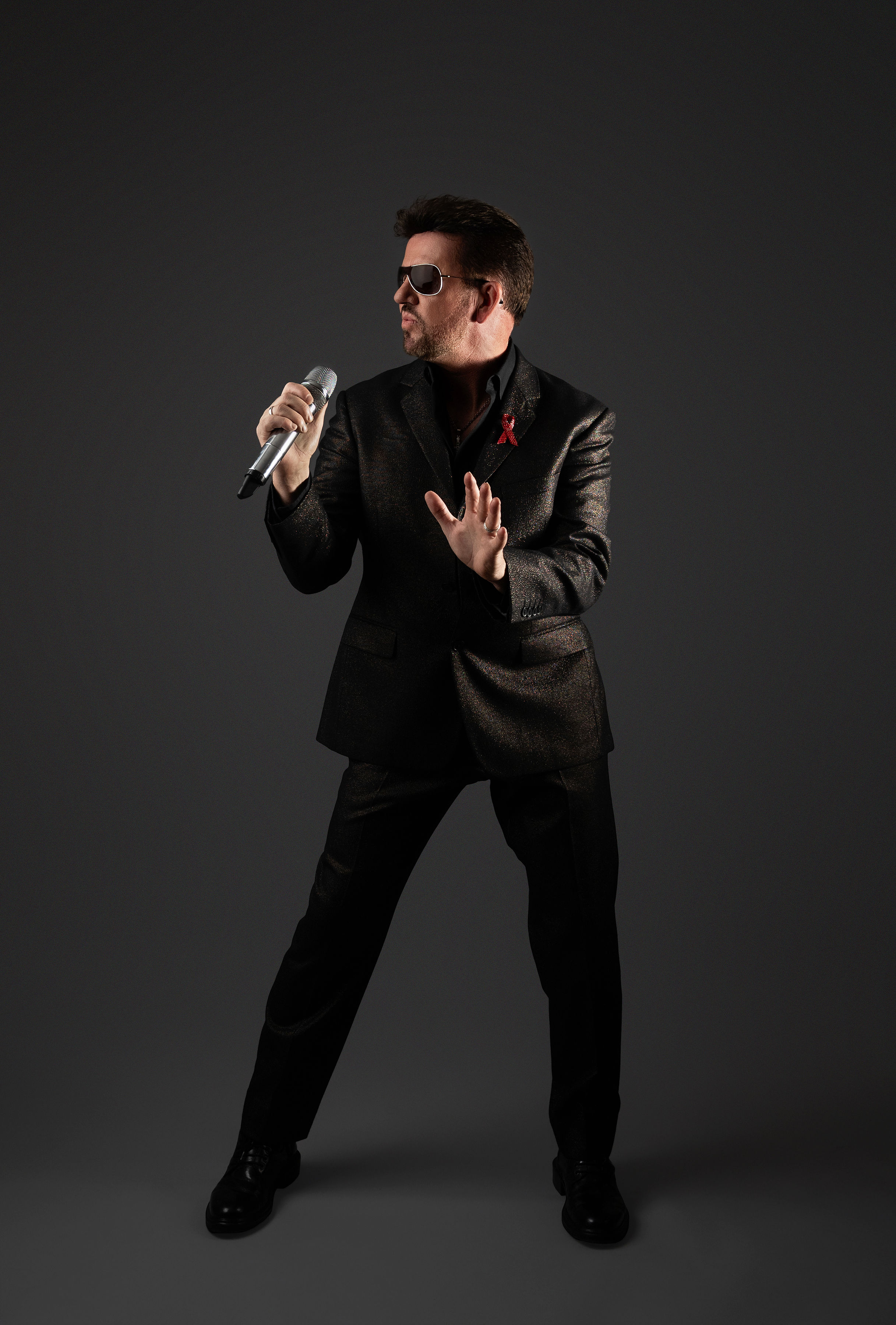 Steve Mitchell in sparkly jacket with hand extended against gray background