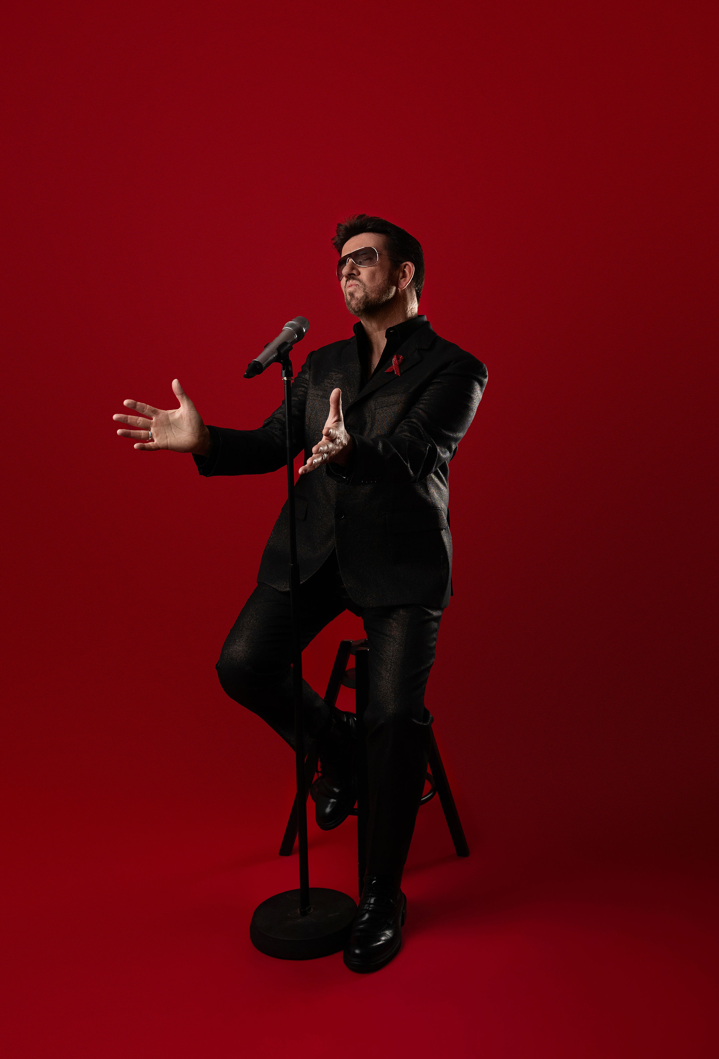 Steve Mitchell with hands outstretched in dramatic pose against red background