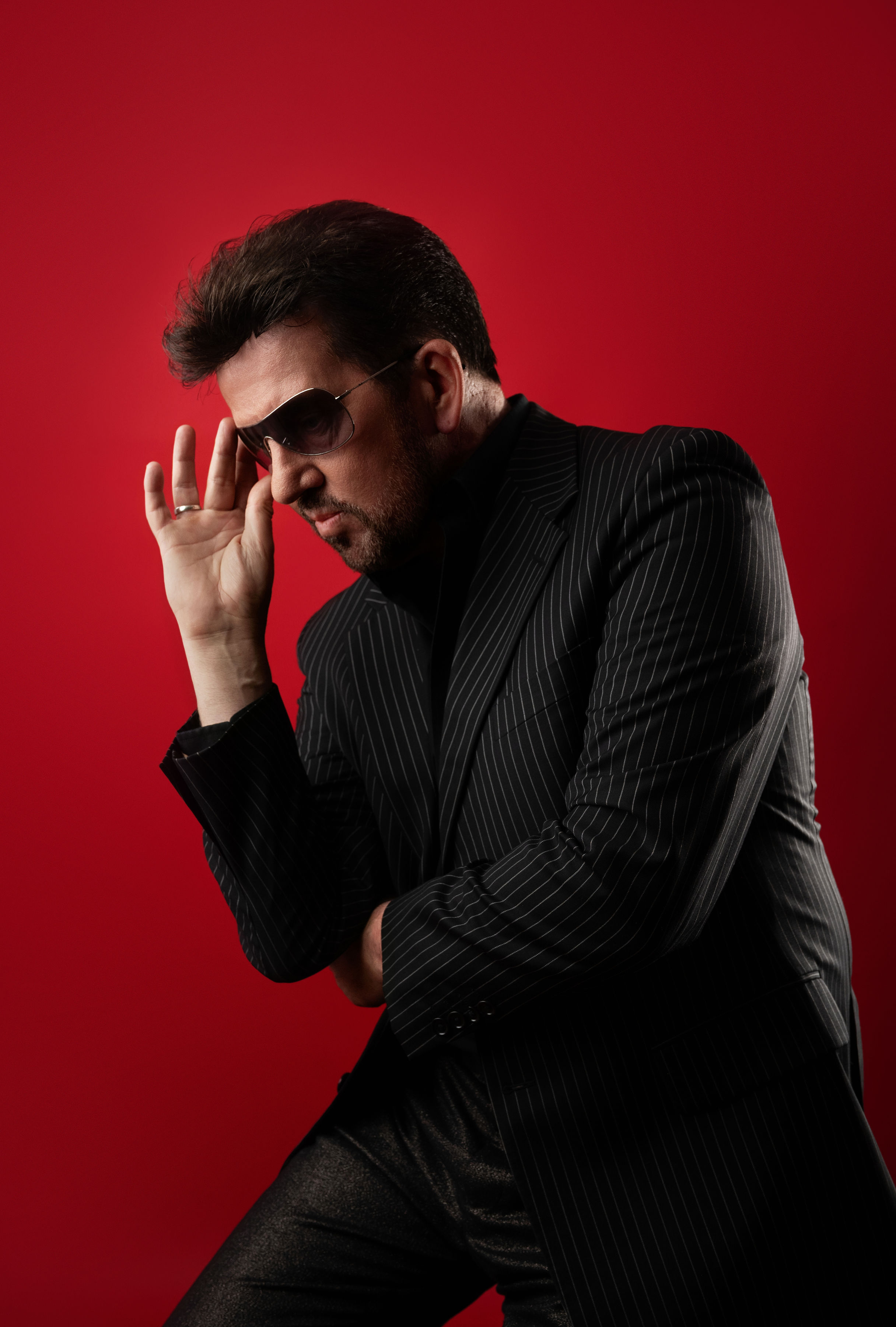 Steve Mitchell in pinstripe suit adjusting sunglasses against red background