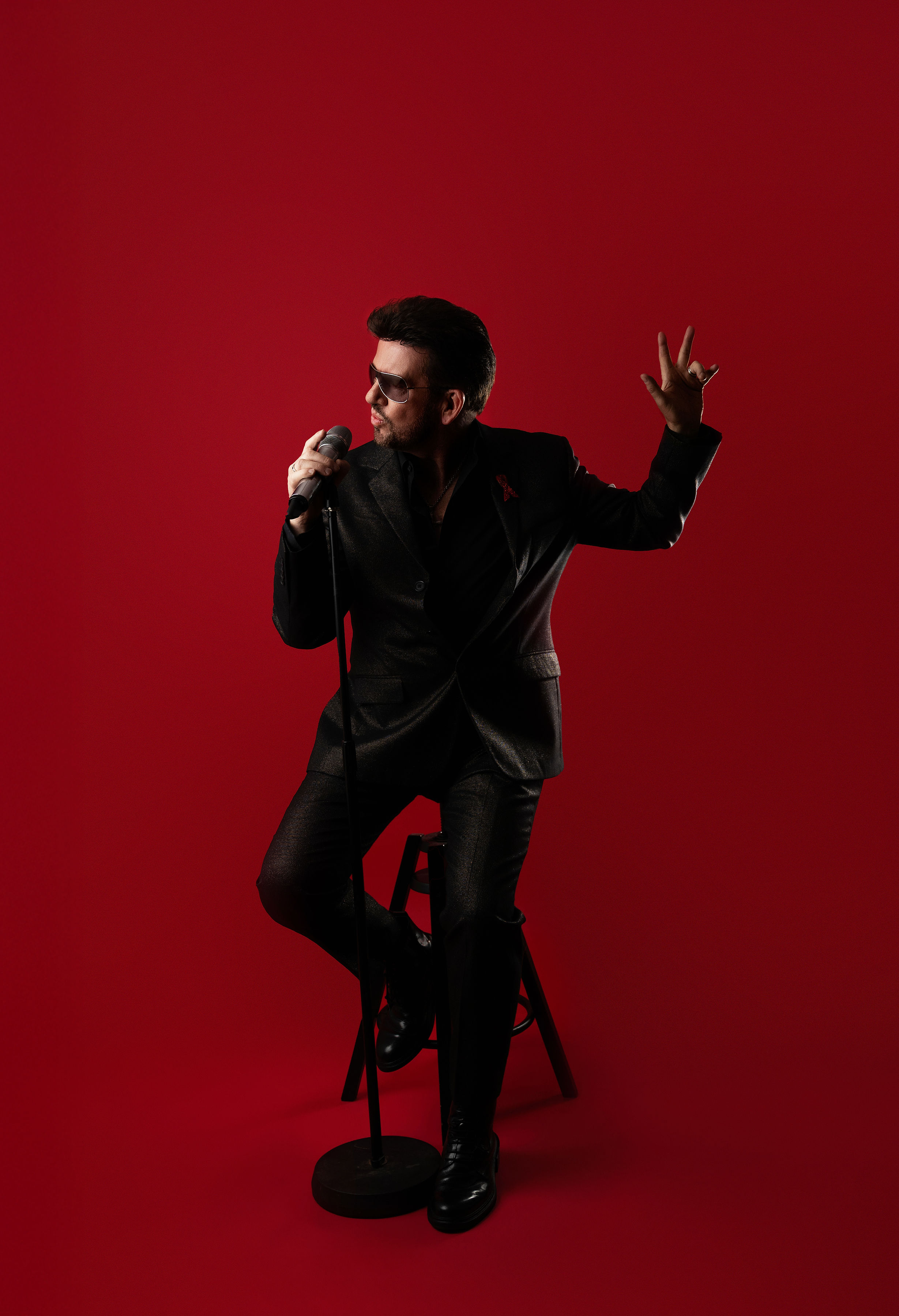 Steve Mitchell sitting on stool singing ballad against red background