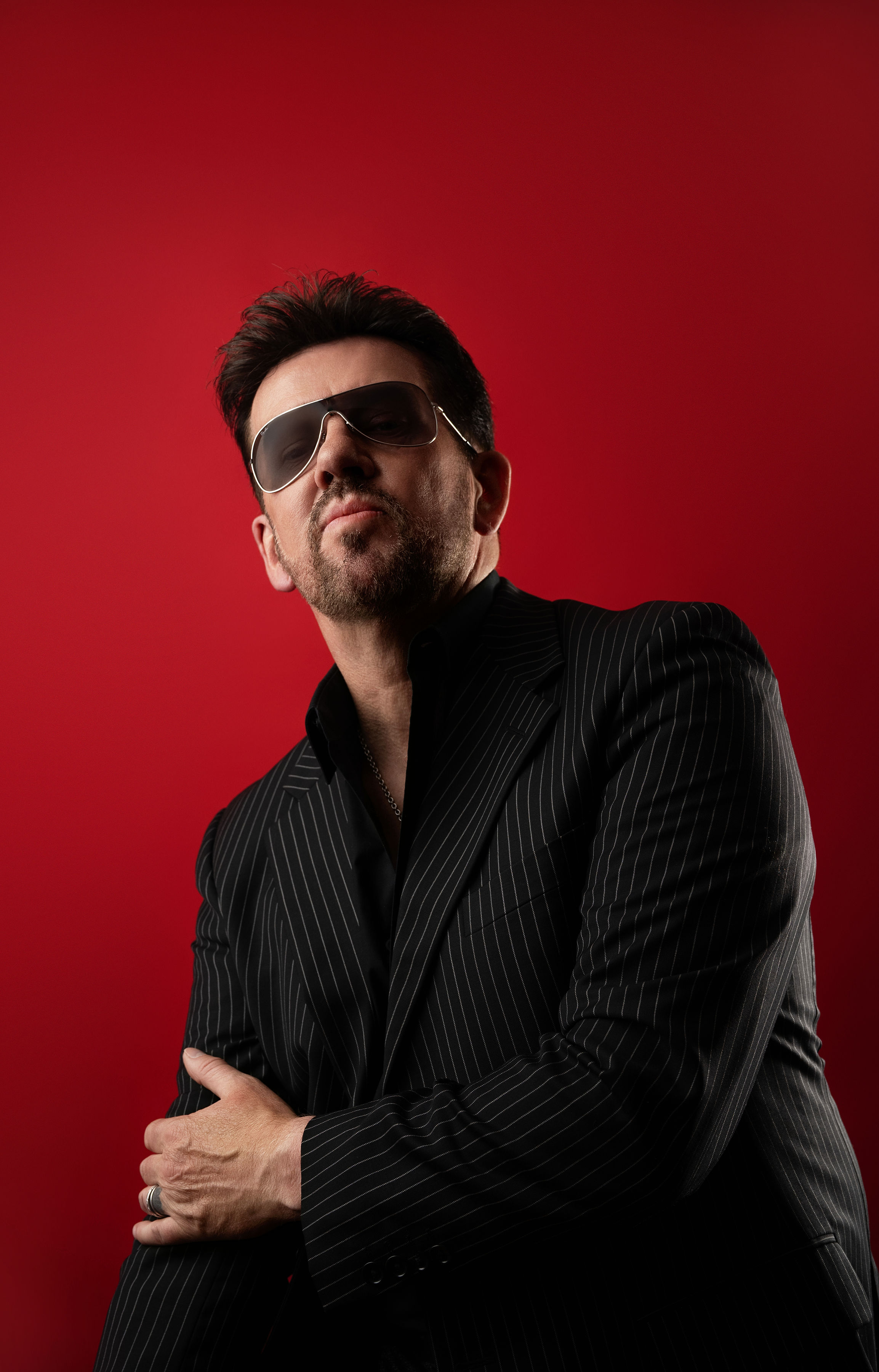 Steve Mitchell in pinstripe suit with arms crossed against red background