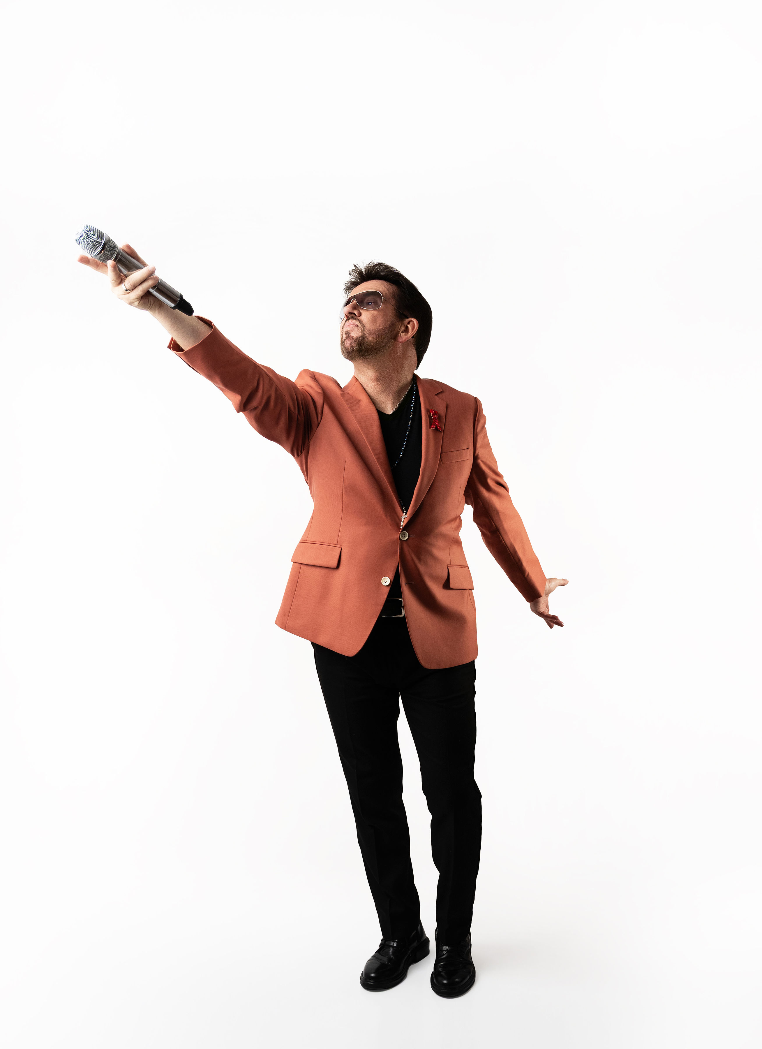 Steve Mitchell in rust colored blazer with arm raised high holding microphone