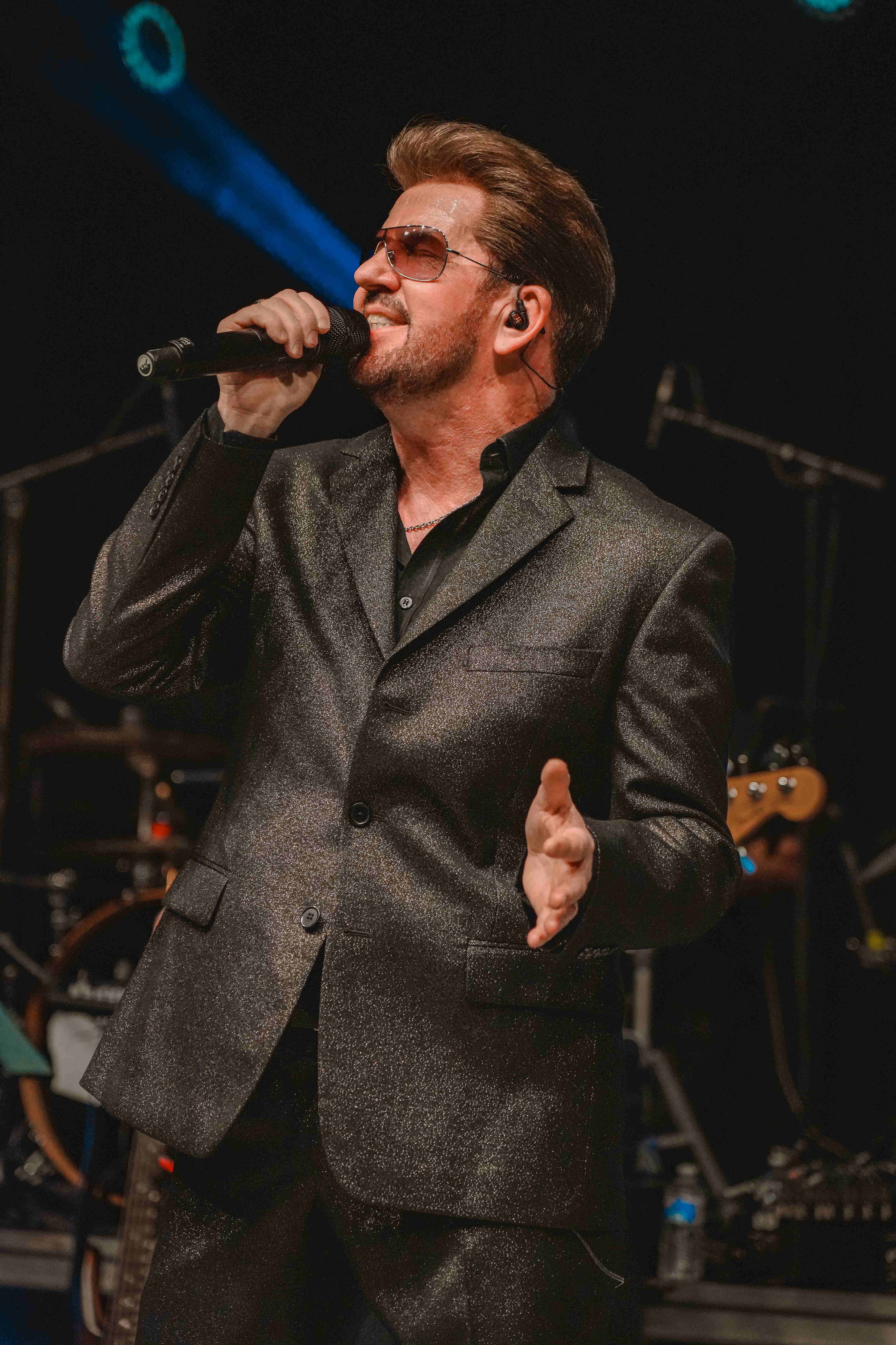Steve Mitchell looking upward while singing, wearing sunglasses and sparkly suit