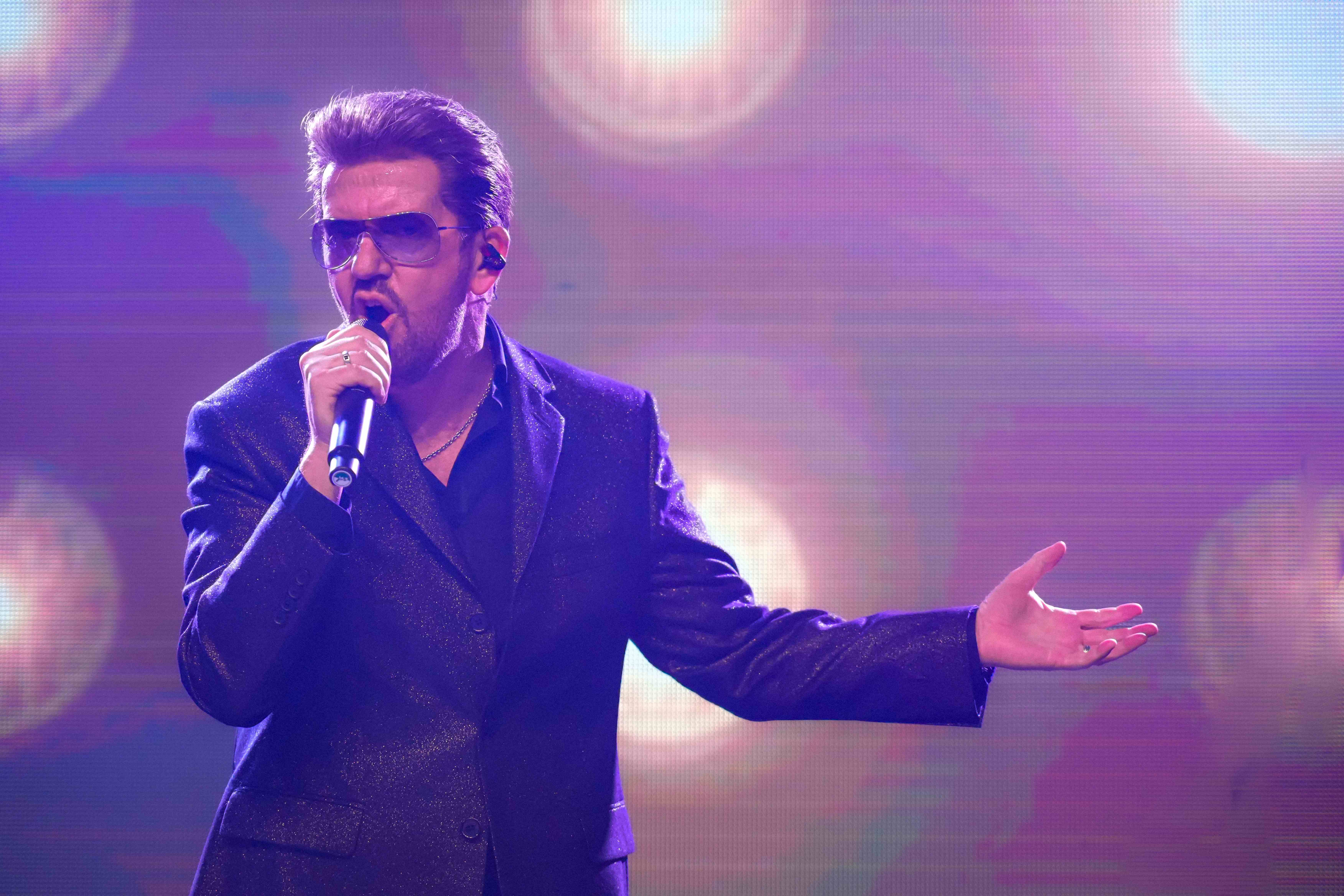 Steve Mitchell performing with outstretched arm against purple starry backdrop