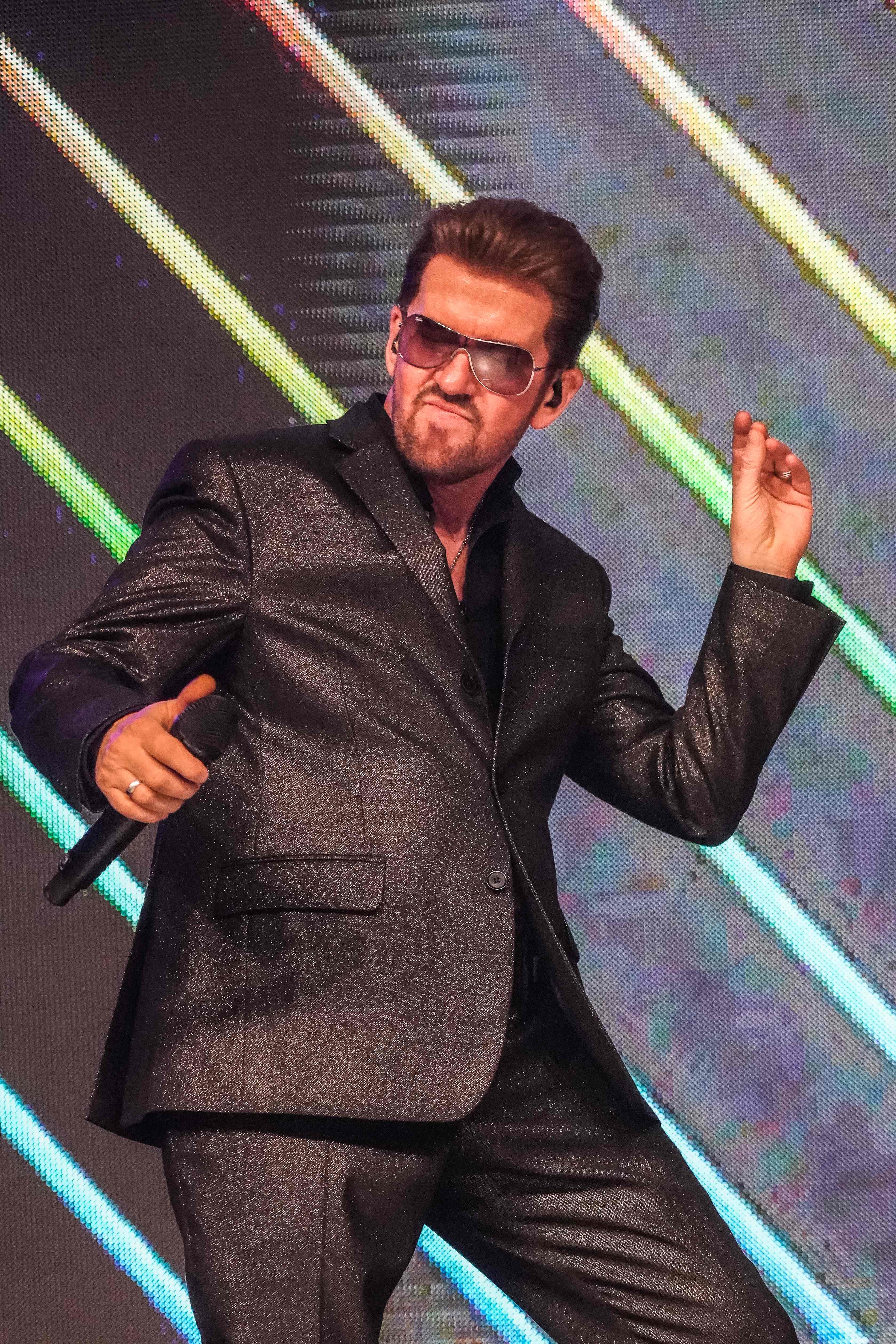 Steve Mitchell performing with sparkly gray suit against colorful striped LED backdrop